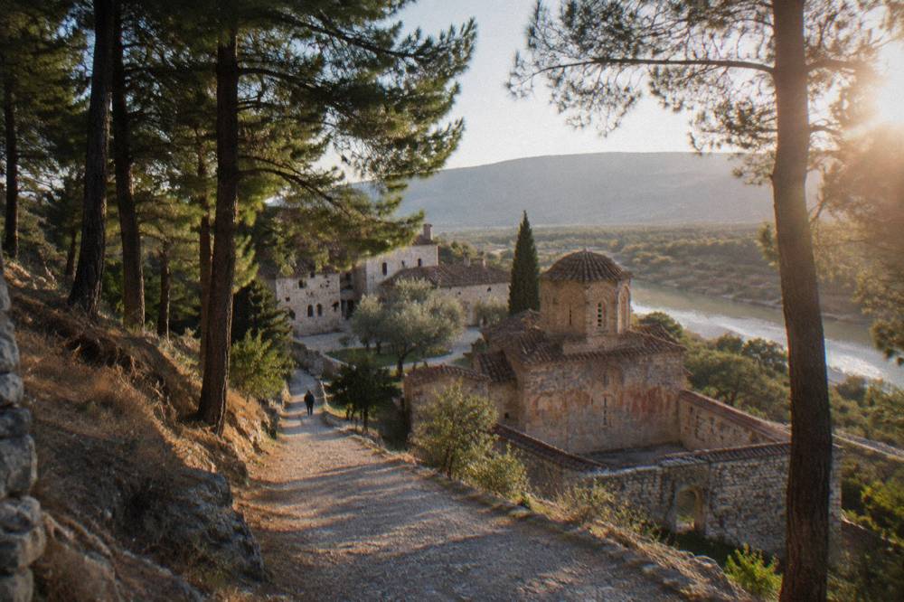 A quiet gravel path leading uphill through pine trees toward monastery buildings