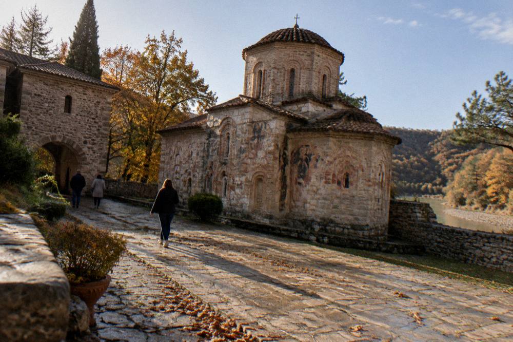 Autumn-colored oak and pine woodland around a stone monastery wall under a clear sky