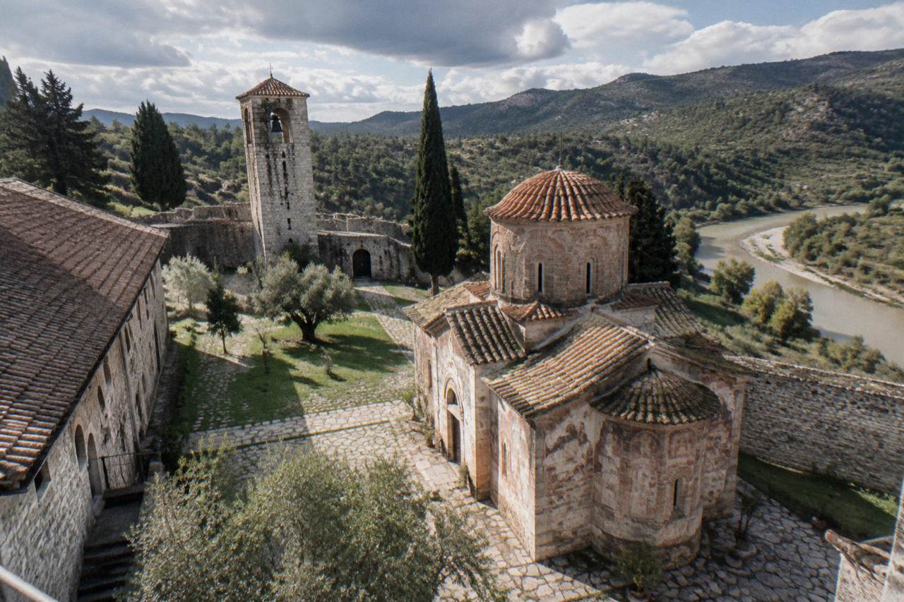 A hilltop monastery with a bell tower and walled courtyard overlooking pine-covered hills