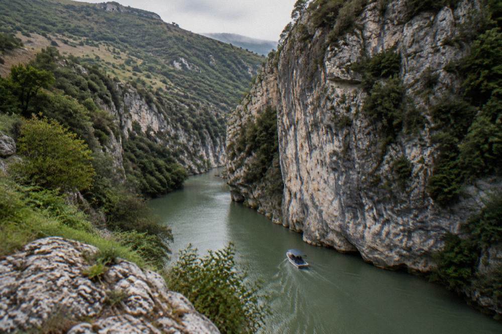 Steep limestone walls of Osum Canyon above green river water with a small boat below