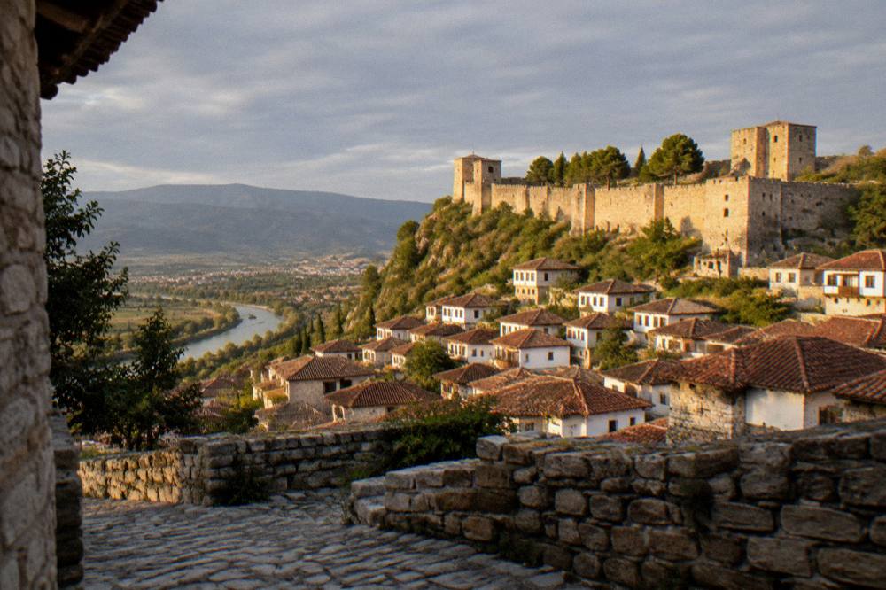 Golden late afternoon light on the stone walls and towers of Berat Castle above the red rooftops
