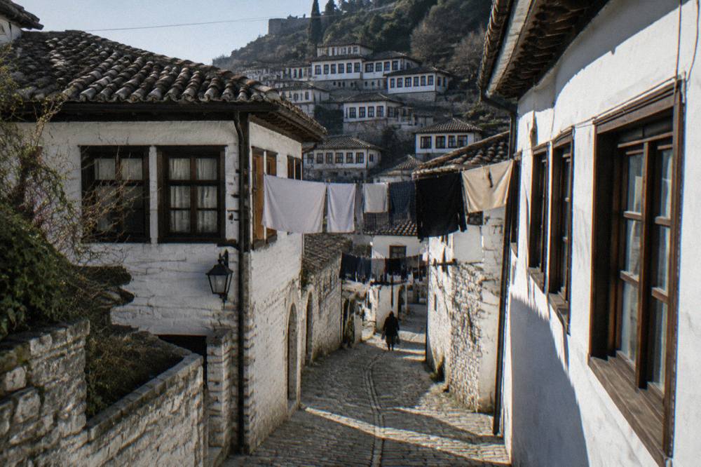 A shaded stone street in Mangalem with laundry overhead and white walls gleaming in the sun