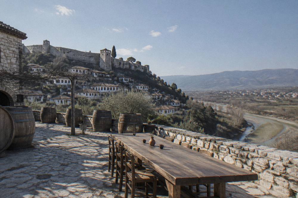 A stone winery courtyard in Berat with oak barrels and a long wooden tasting table