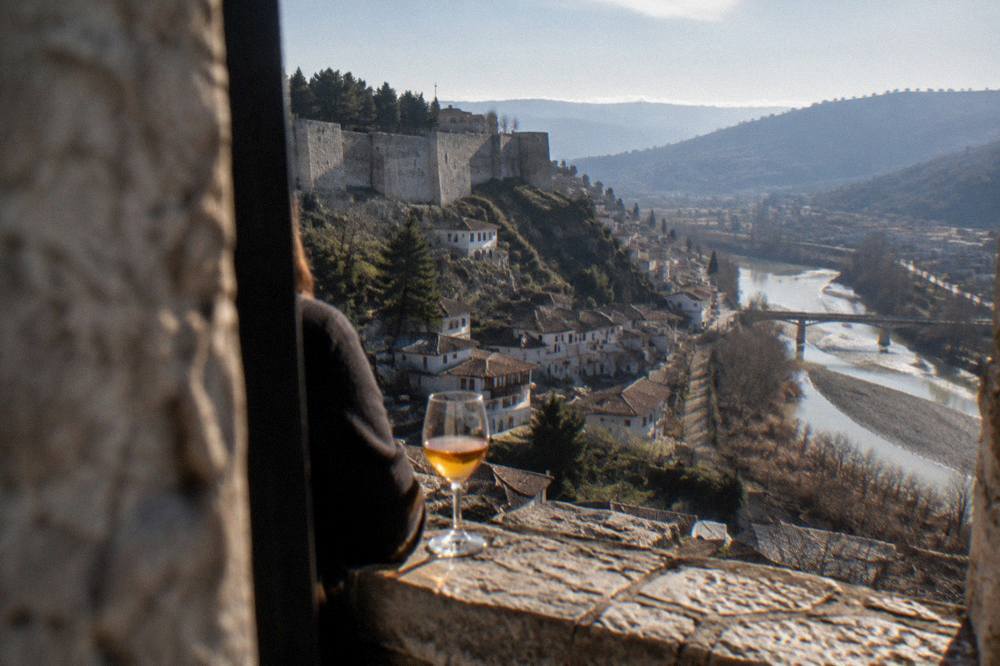A glass of amber local wine on a stone windowsill overlooking the Osum River in Berat