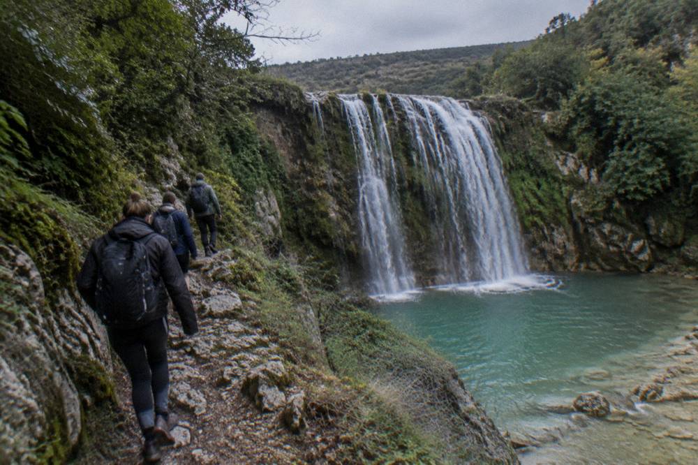 A guide leading a small group along a rocky path above a turquoise river gorge