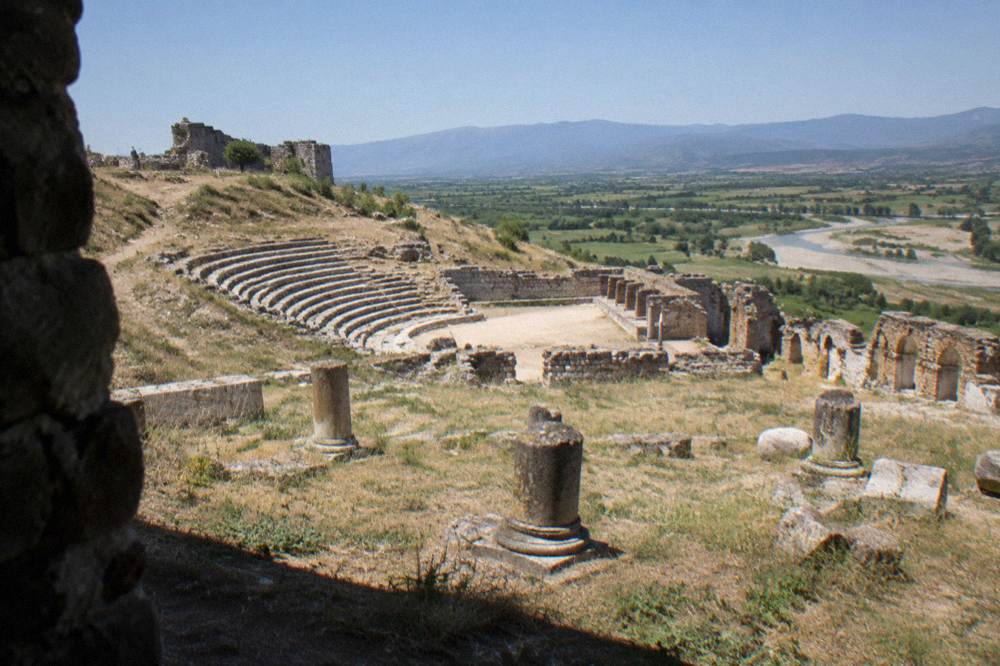 Ancient stone ruins of a hilltop city standing above a wide green plain under a clear sky