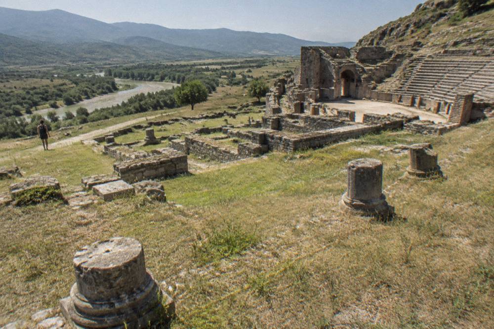 Rows of ancient stone foundations of buildings laid out on a grassy hilltop plateau
