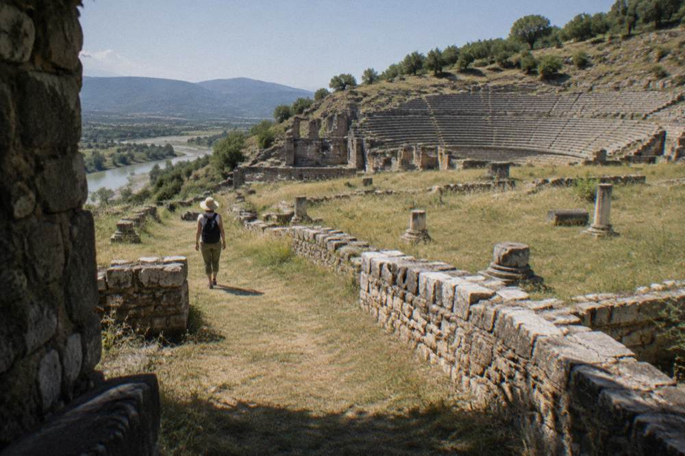 A visitor in a sun hat walking a wide grassy path between ancient stone walls under bright sun