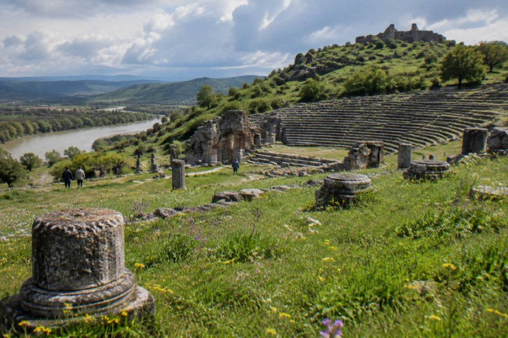 Rolling green hills with wildflowers in foreground and ruins on a distant hill under spring clouds
