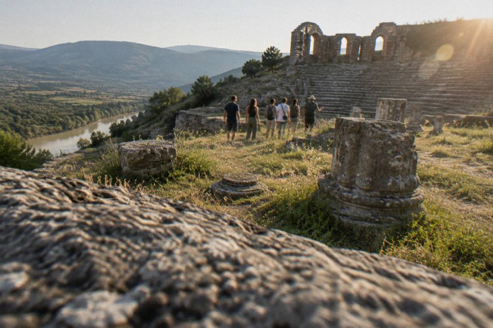A small group of visitors walking with a guide among ancient stone ruins in morning light