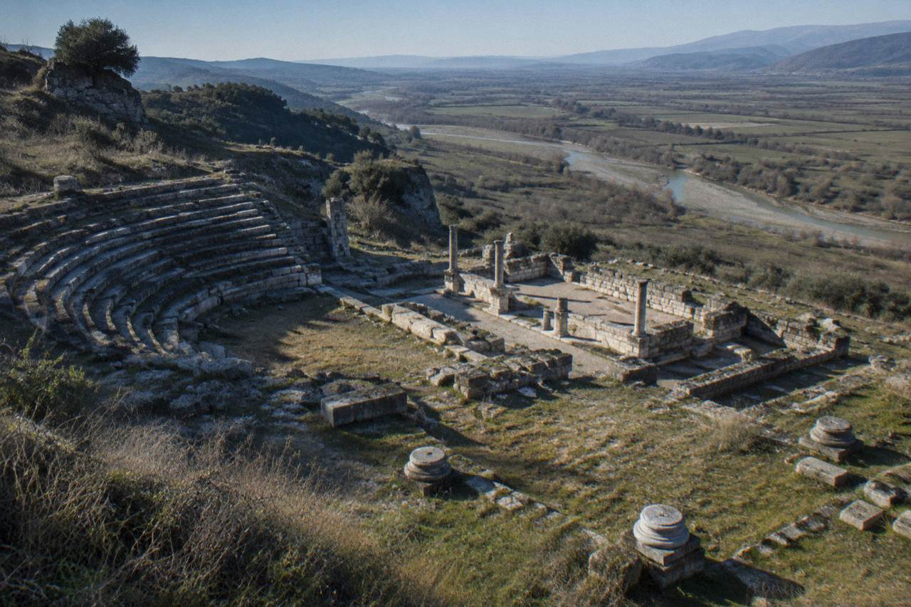 Ancient stone ruins of a hilltop city standing above a wide green plain under a clear sky