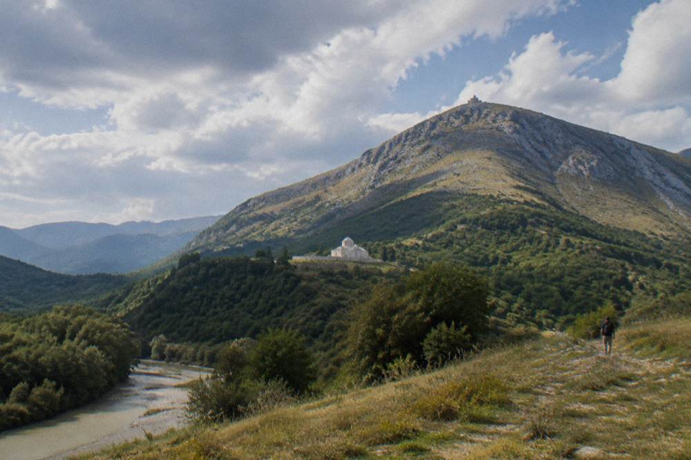 A white stone tekke building on a high green saddle below the Tomorr summit