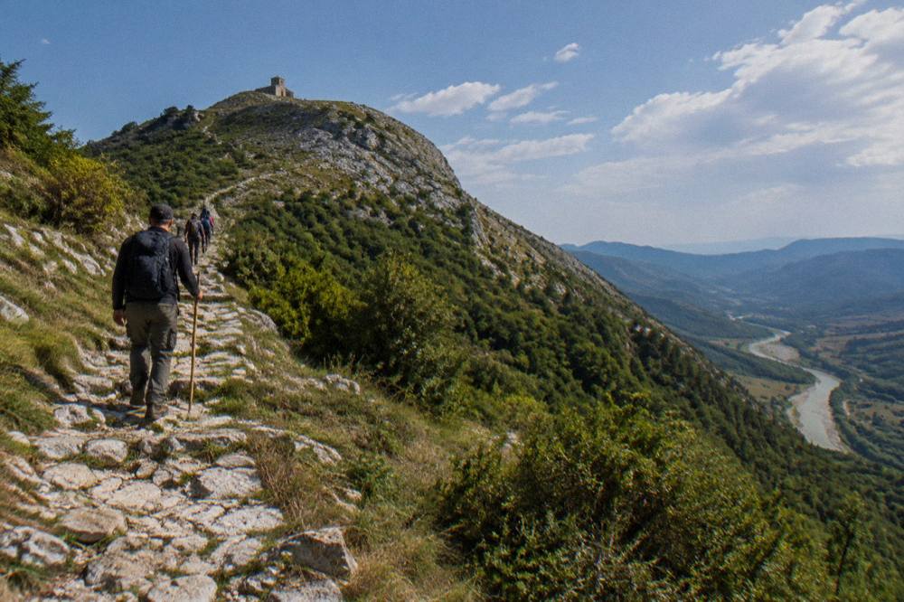 A local guide leading walkers along a stone path toward the Tomorr highlands