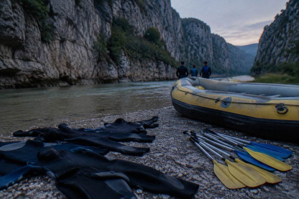 Wetsuits and paddles laid out on a riverbank before a rafting trip