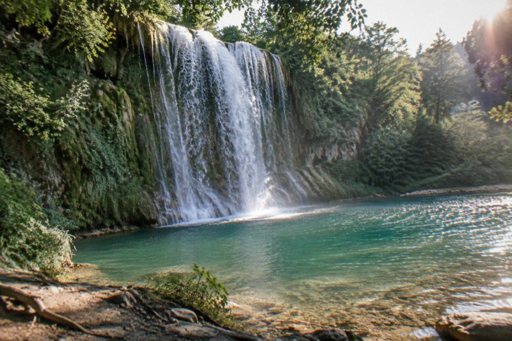Bogove waterfall falling into a clear pool surrounded by green forest