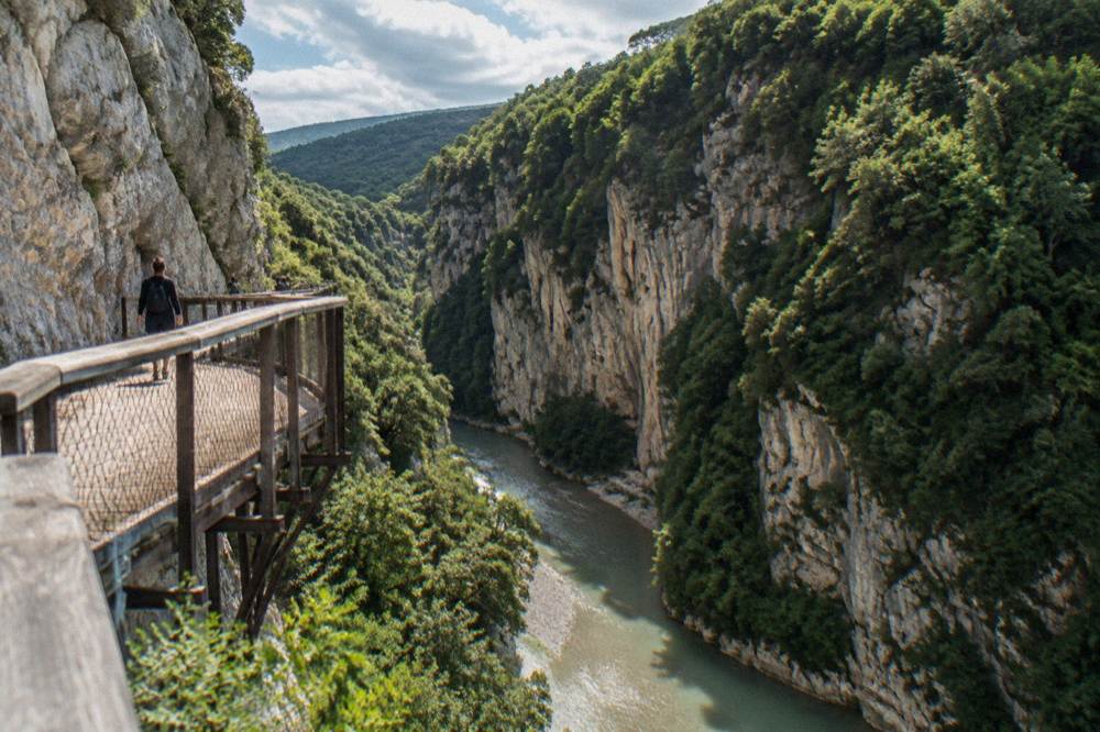 A deep limestone river gorge with steep forested walls and green water running along the canyon floor