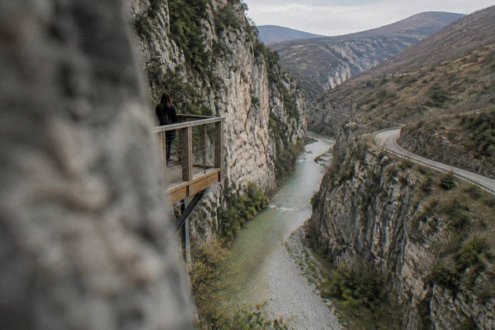 A winding asphalt road through bare hills descending toward a river valley with a distant gorge