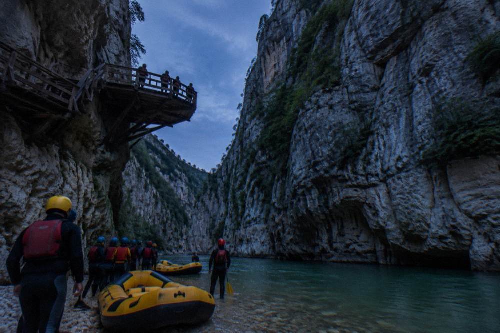 Inflatable rafts and groups in helmets and wetsuits preparing beside green river water below canyon walls