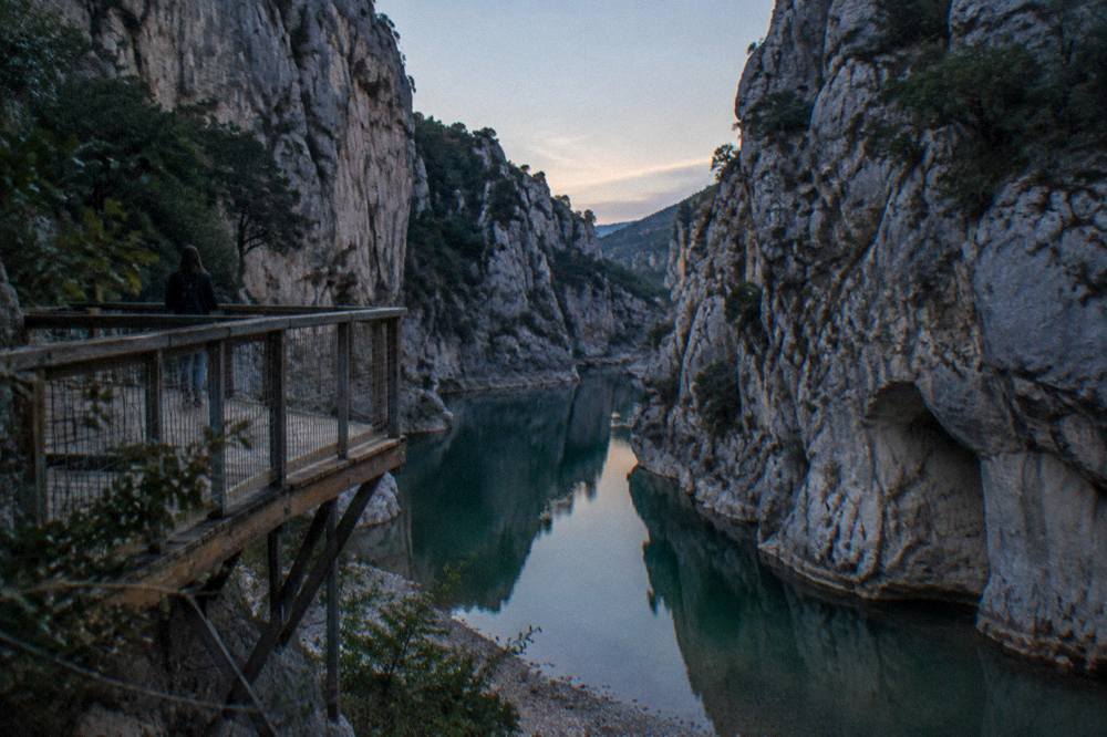 A calm green river pool between narrow rock walls reflecting the cliffs above