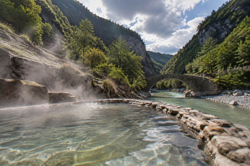Small stone bridge over a turquoise river canyon with forested cliffs rising on both sides
