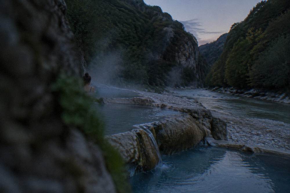 Steaming water trickling over pale rock into natural pools at the mouth of a narrow canyon