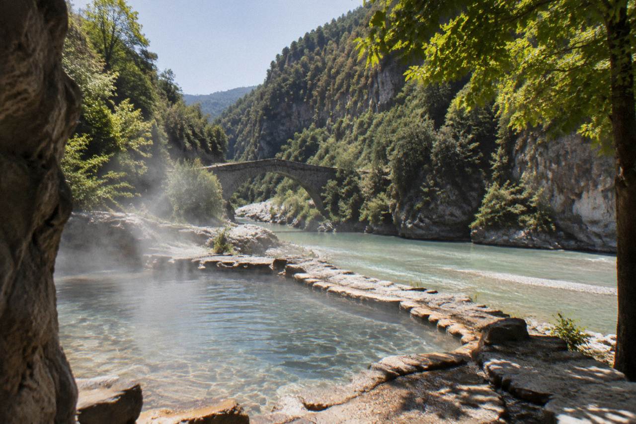 Small stone bridge over a turquoise river canyon with forested cliffs rising on both sides