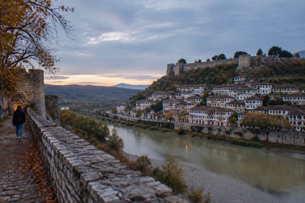White Ottoman houses with rows of windows stacked on a hillside in Berat, seen across the river in autumn light.