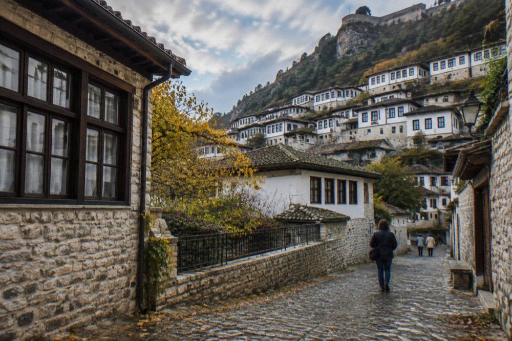 Cobblestone street between old stone houses in the Mangalem quarter of Berat under a partly cloudy autumn sky.