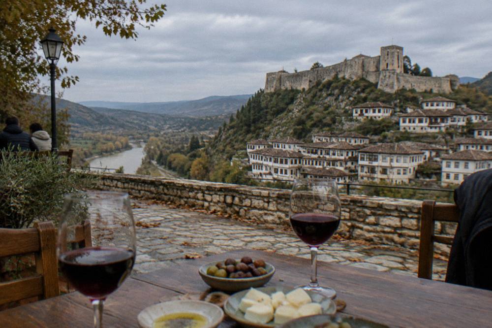 Glasses of red wine and small plates of cheese and olives on a wooden table in a Berat restaurant.