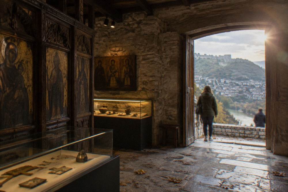 Interior of a small museum in Berat with wooden icon screens and lit display cases along stone walls.