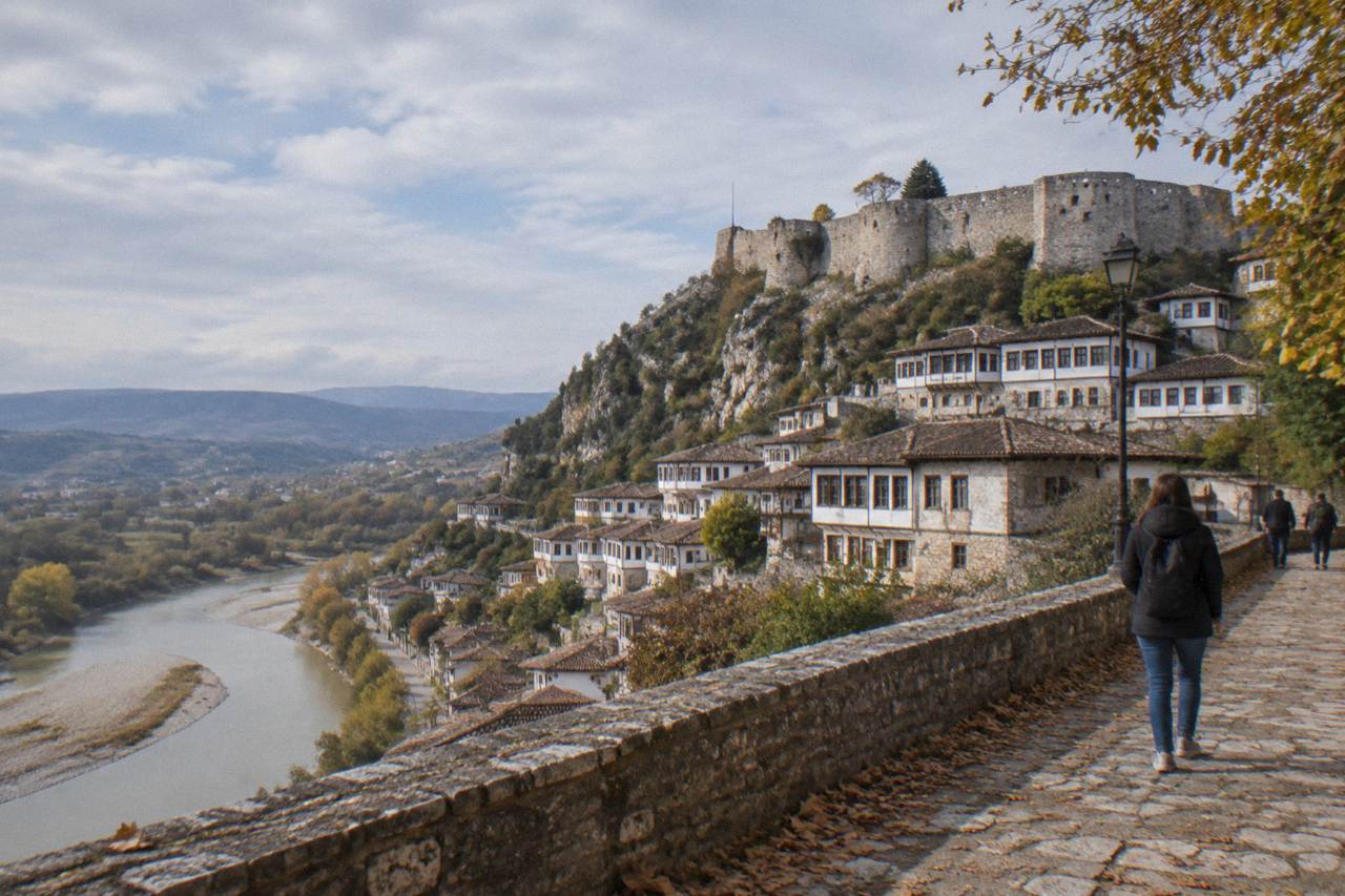 Ottoman-era houses stacked on a hillside above a river in Berat, Albania, under a soft autumn sky.