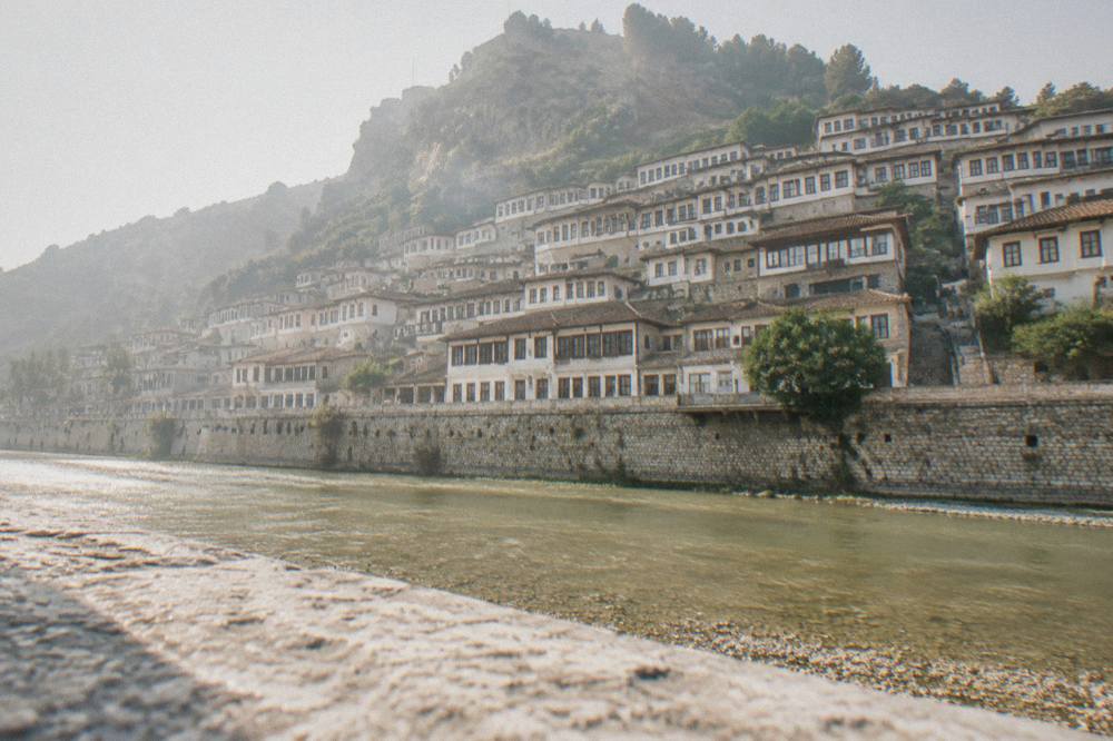 Stacked whitewashed Ottoman houses of the Mangalem quarter seen from the flat riverbank below