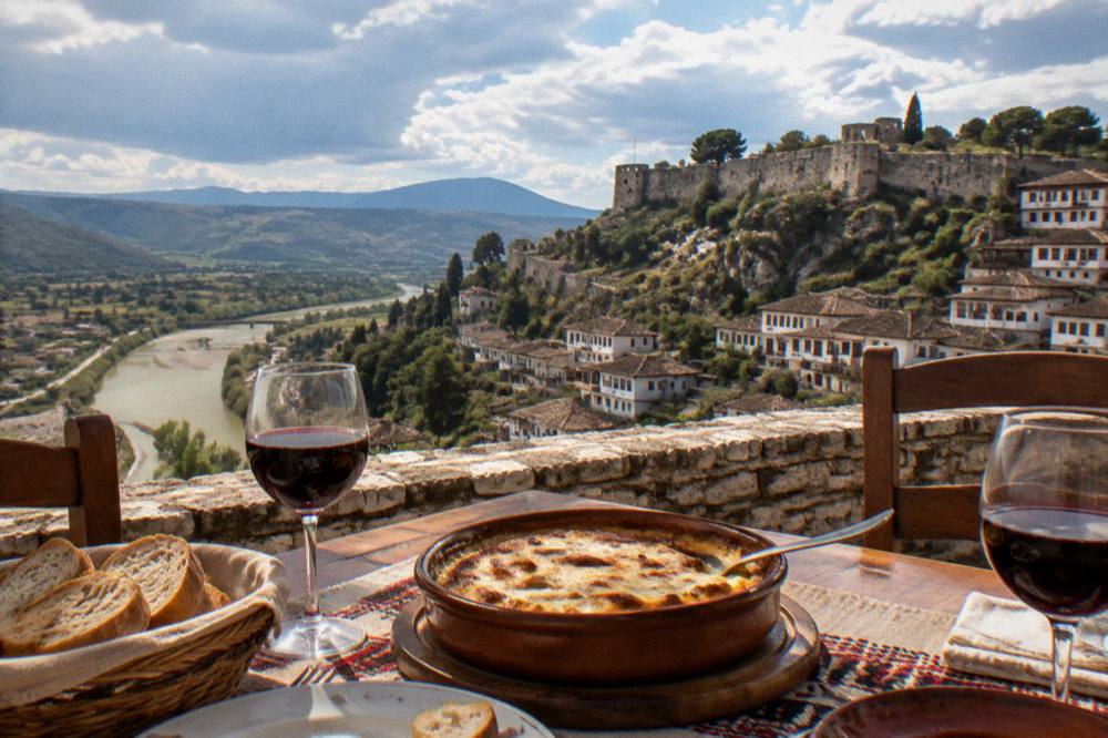 Traditional Albanian restaurant table with tavë kosi, bread and glasses of local wine