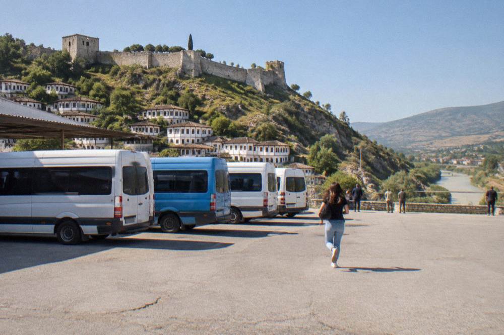 A small regional bus terminal forecourt with several minibuses parked in a row under a clear morning sky