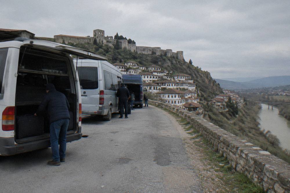A row of parked regional minibuses at a roadside terminal with drivers loading luggage into a rear compartment