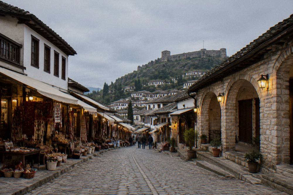 A narrow old town lane lit by warm lamps at dusk with stone walls and closed wooden shutters