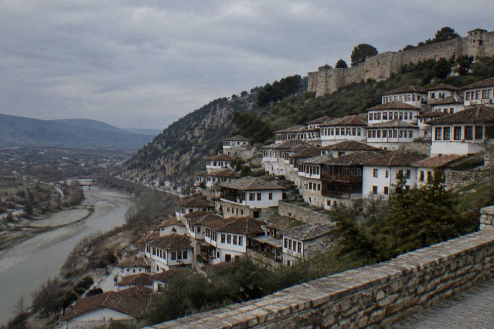 A hillside of white Ottoman houses with dense rows of windows rising toward stone castle walls in late afternoon light