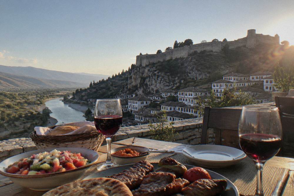 A table with Balkan grilled food, salad and glasses of red wine at a restaurant in Berat