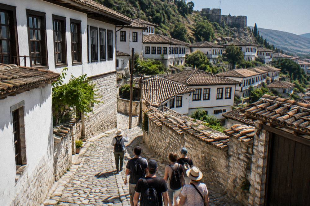 A guide leading a small group of visitors along a cobbled street in Mangalem, Berat