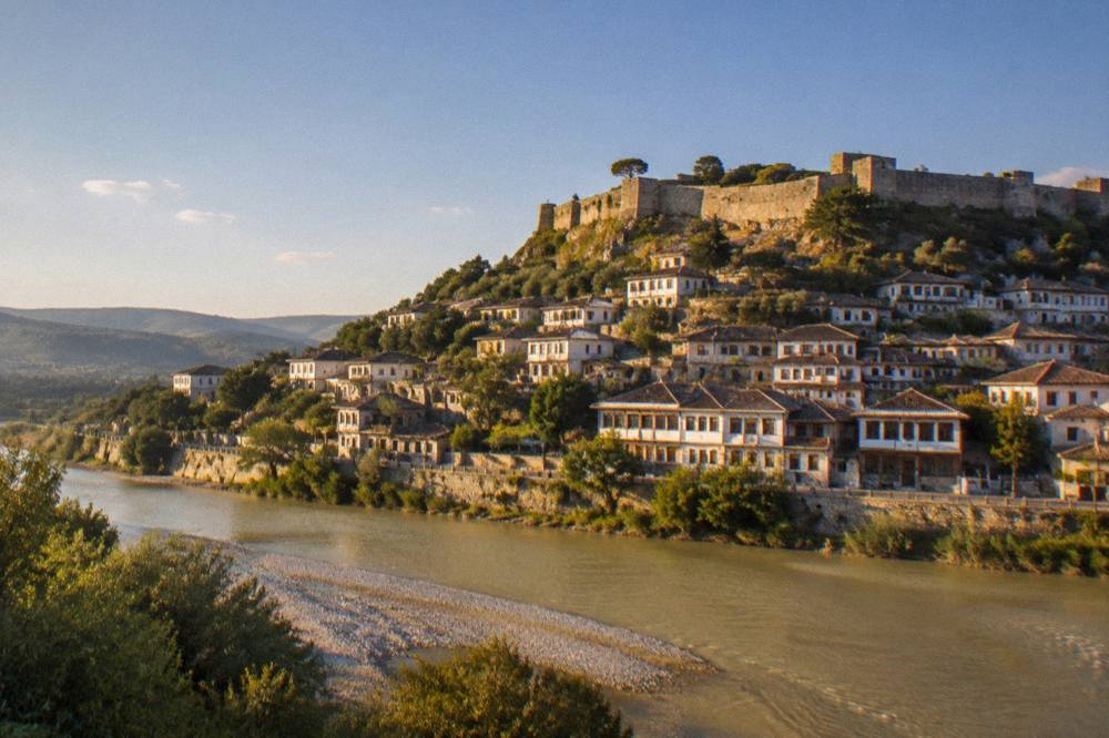 Berat at dusk seen from across the Osum River, with the castle lit above the town