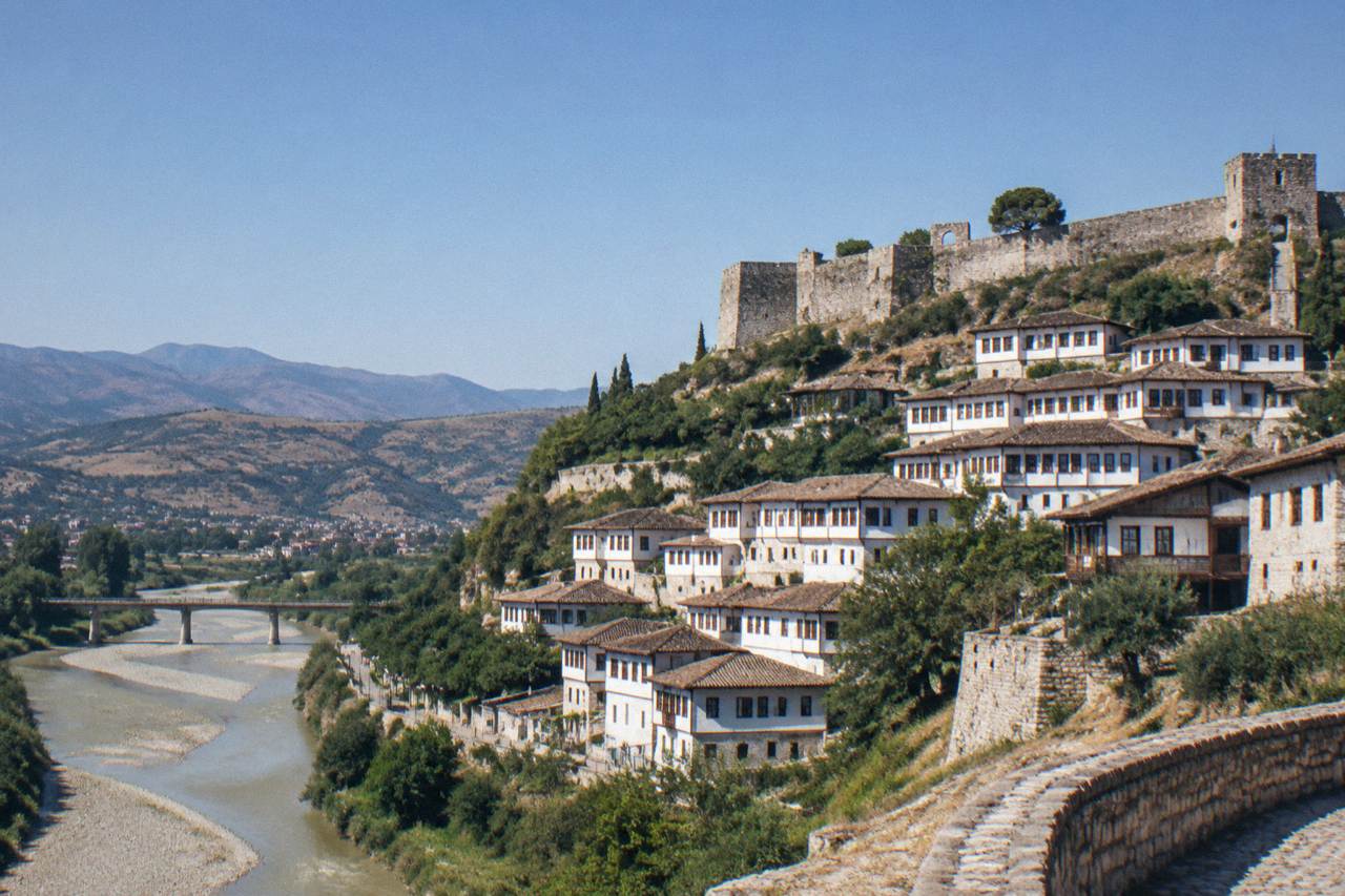 White Ottoman-era houses stacked on a hillside below a stone castle wall in Berat, Albania