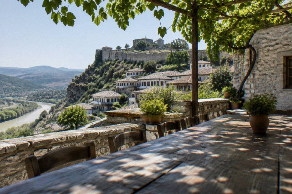 A guesthouse courtyard in Berat with stone walls, grapevines, and a long wooden table