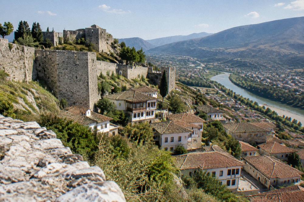 The stone walls and towers of Berat Castle above red-tiled rooftops