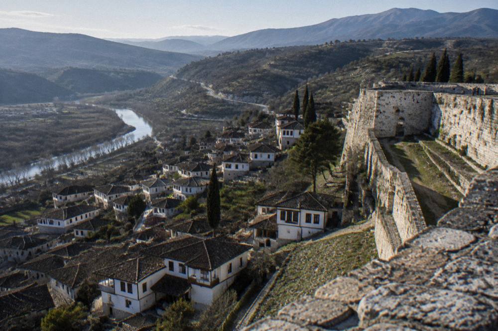 Winding road through green hills toward high mountains on the edge of the Berat region