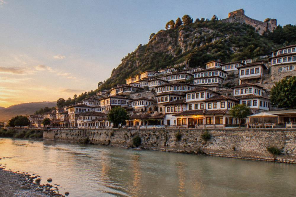 Illuminated Ottoman houses of Mangalem rising above the Osum River at dusk in Berat, Albania