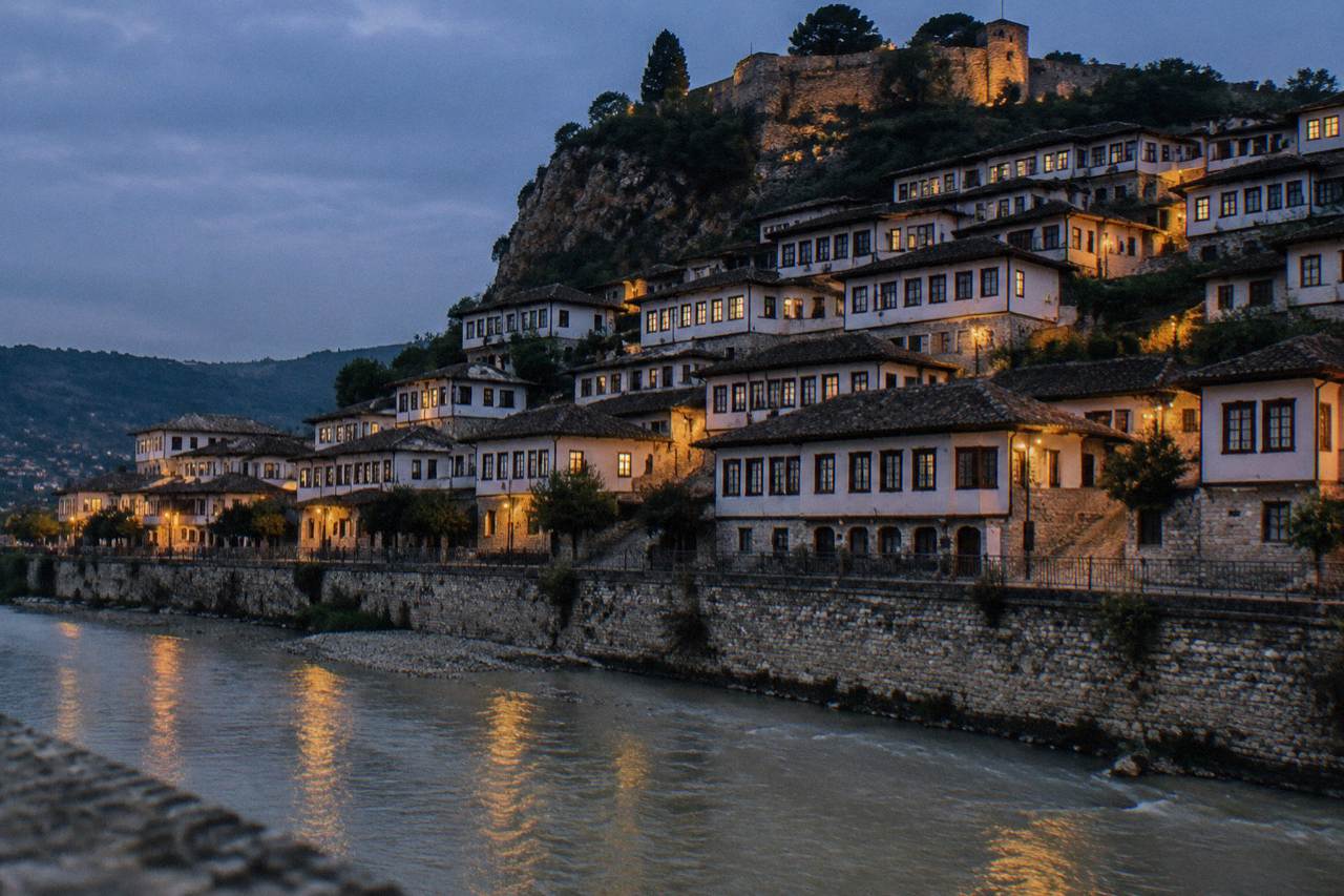 Illuminated Ottoman houses of Mangalem rising above the Osum River at dusk in Berat, Albania
