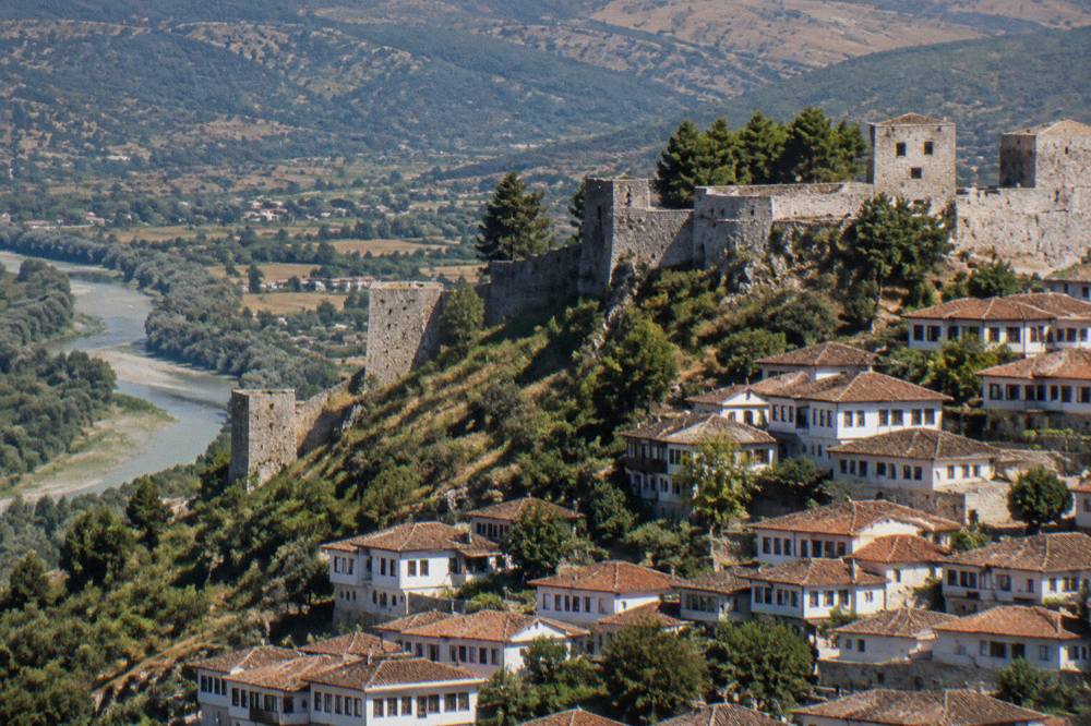Stone walls and towers of Berat Castle above the red tiled roofs of the old town