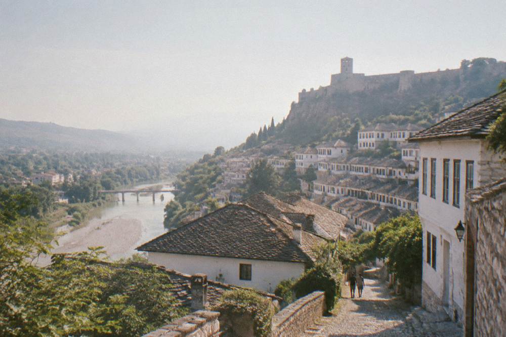 White Ottoman houses stacked on a hillside above a river in an Albanian town