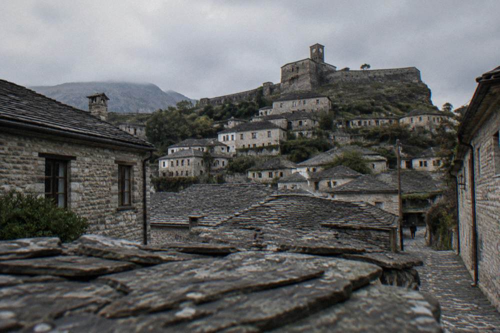 Grey stone houses with slate roofs on a steep hillside beneath a castle
