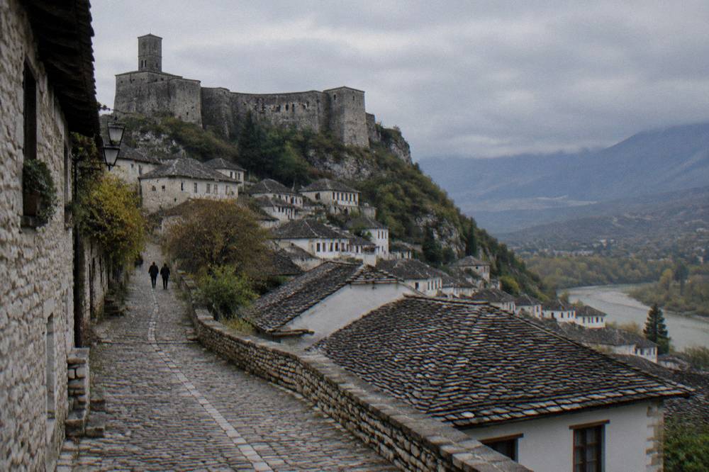 Cobblestone lane leading up to stone castle walls above tiled rooftops